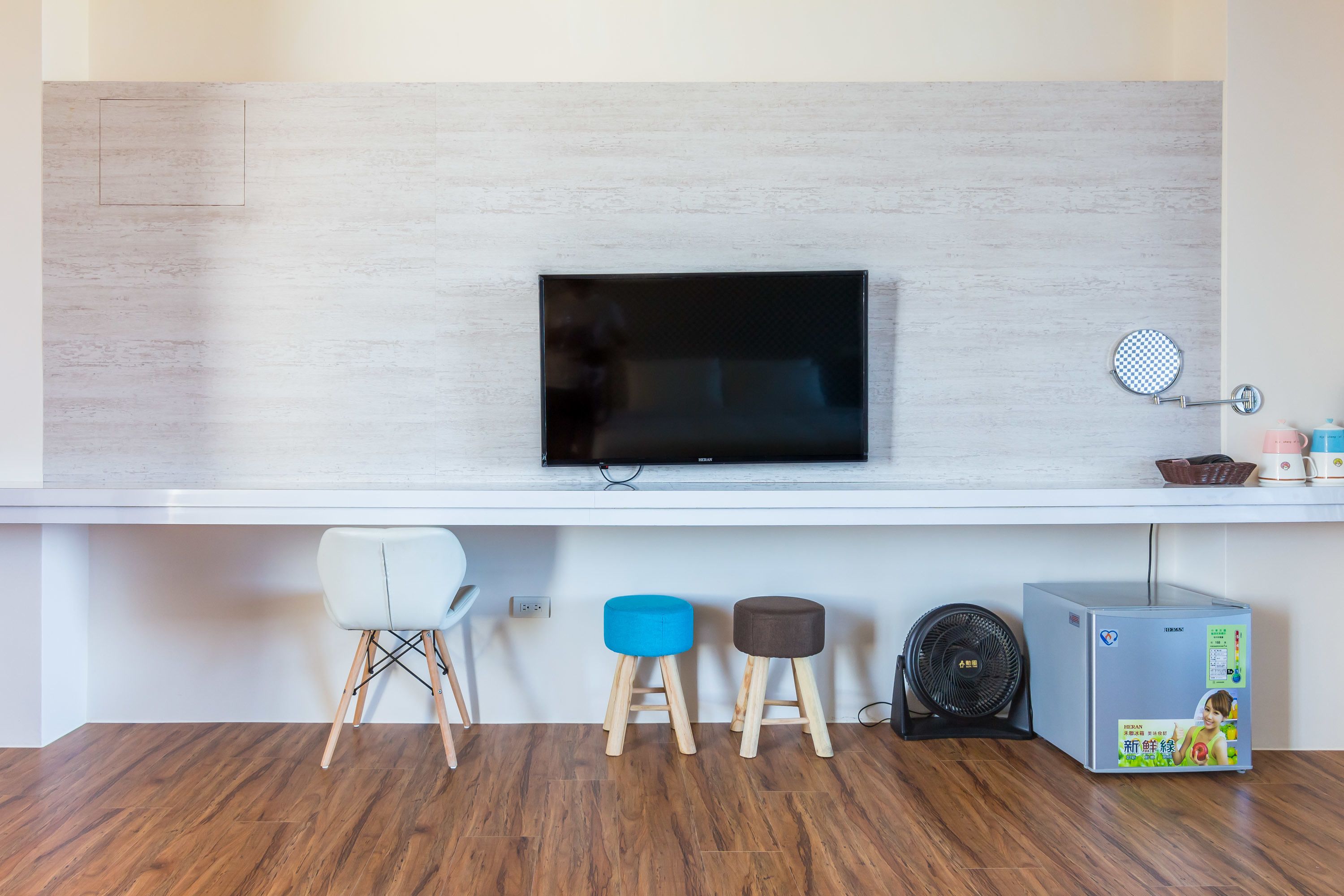 Una cocina moderna con un televisor de pantalla plana en la pared, taburetes de madera, un refrigerador pequeño y un ventilador.