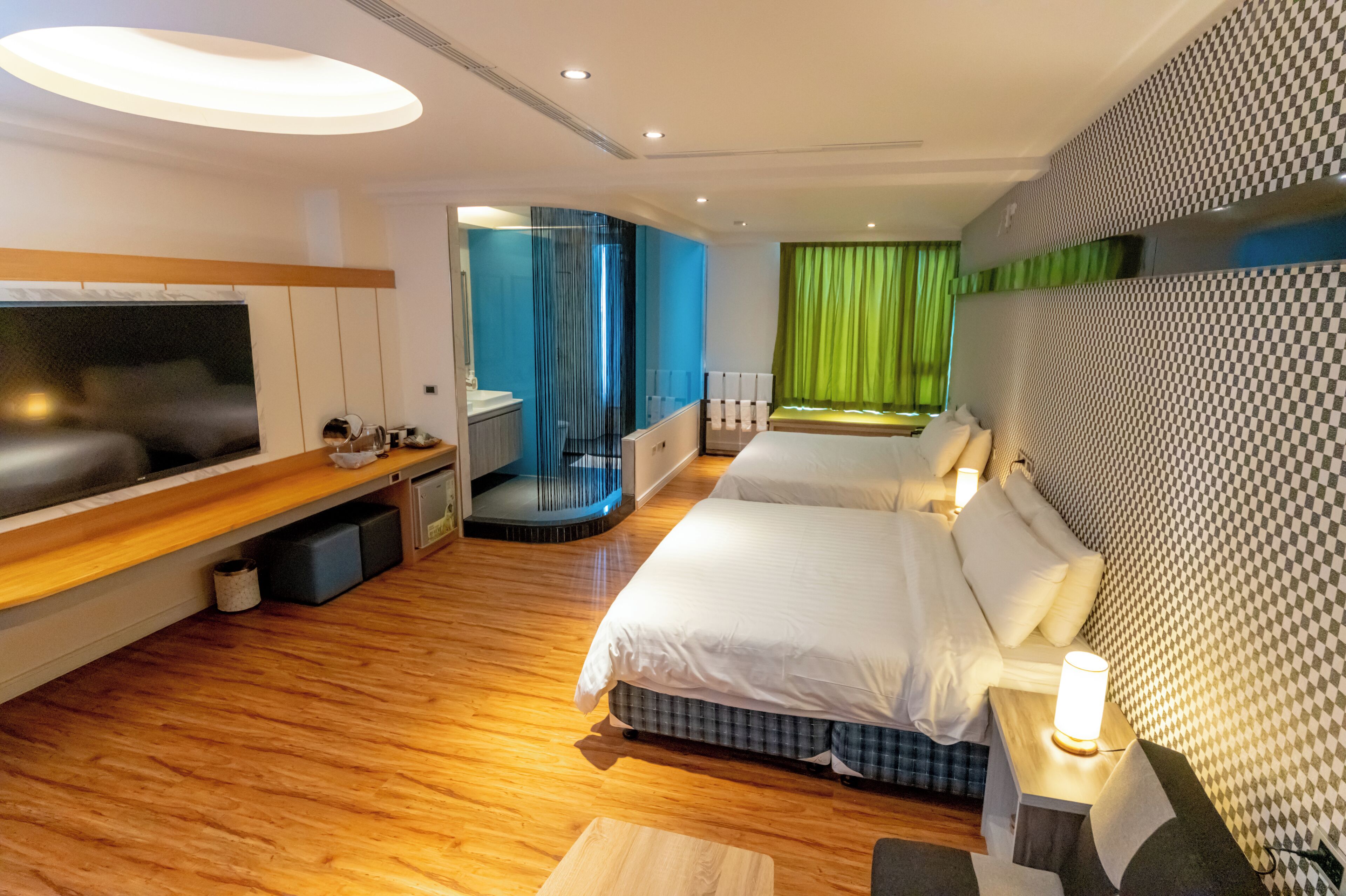 A modern hotel room with a large bed, a TV, a desk, and a seating area with a view of the city.