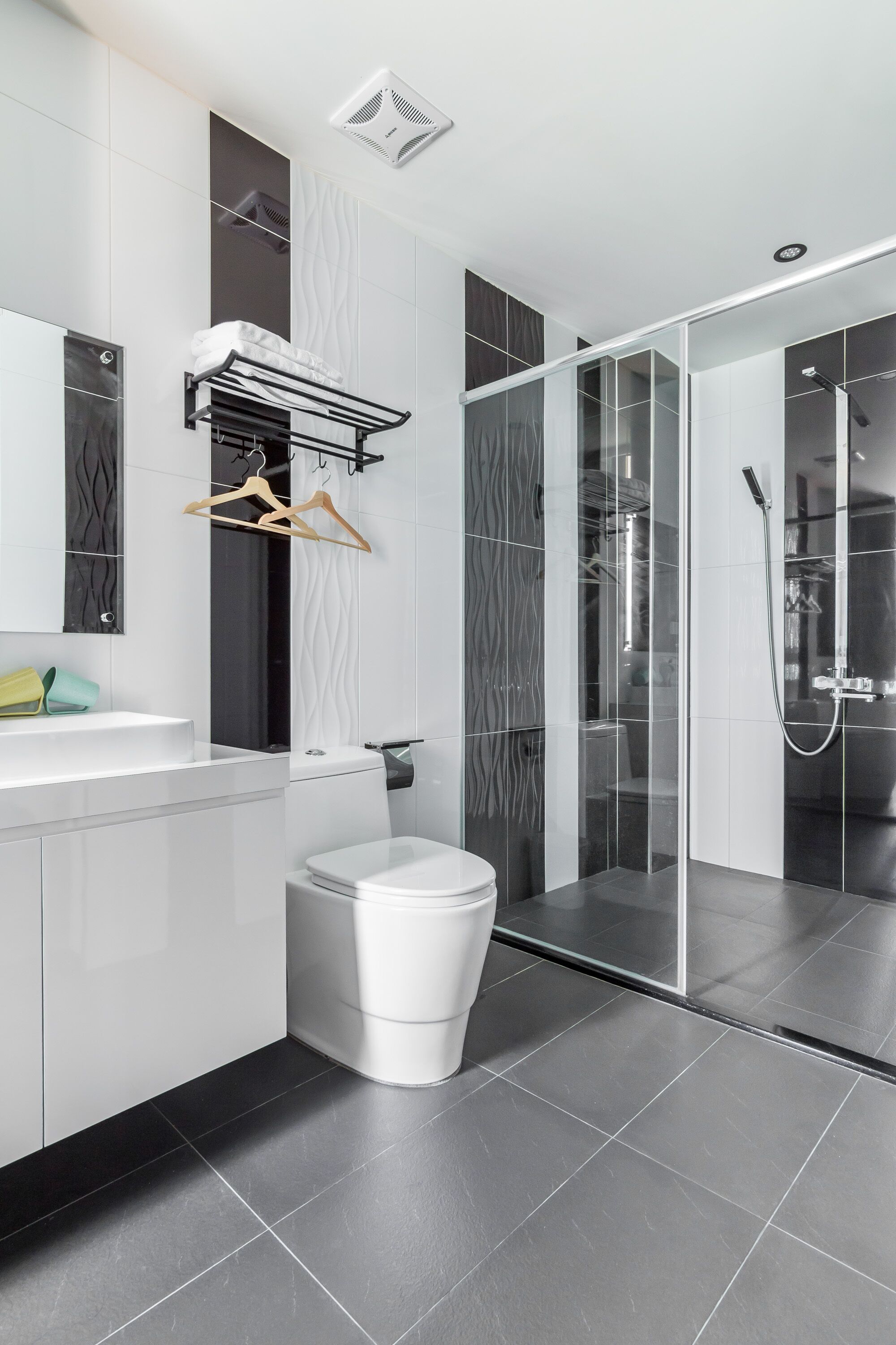 Un bagno moderno con un water bianco, una doccia con pareti in vetro e un lavandino bianco con un porta asciugamani sopra.