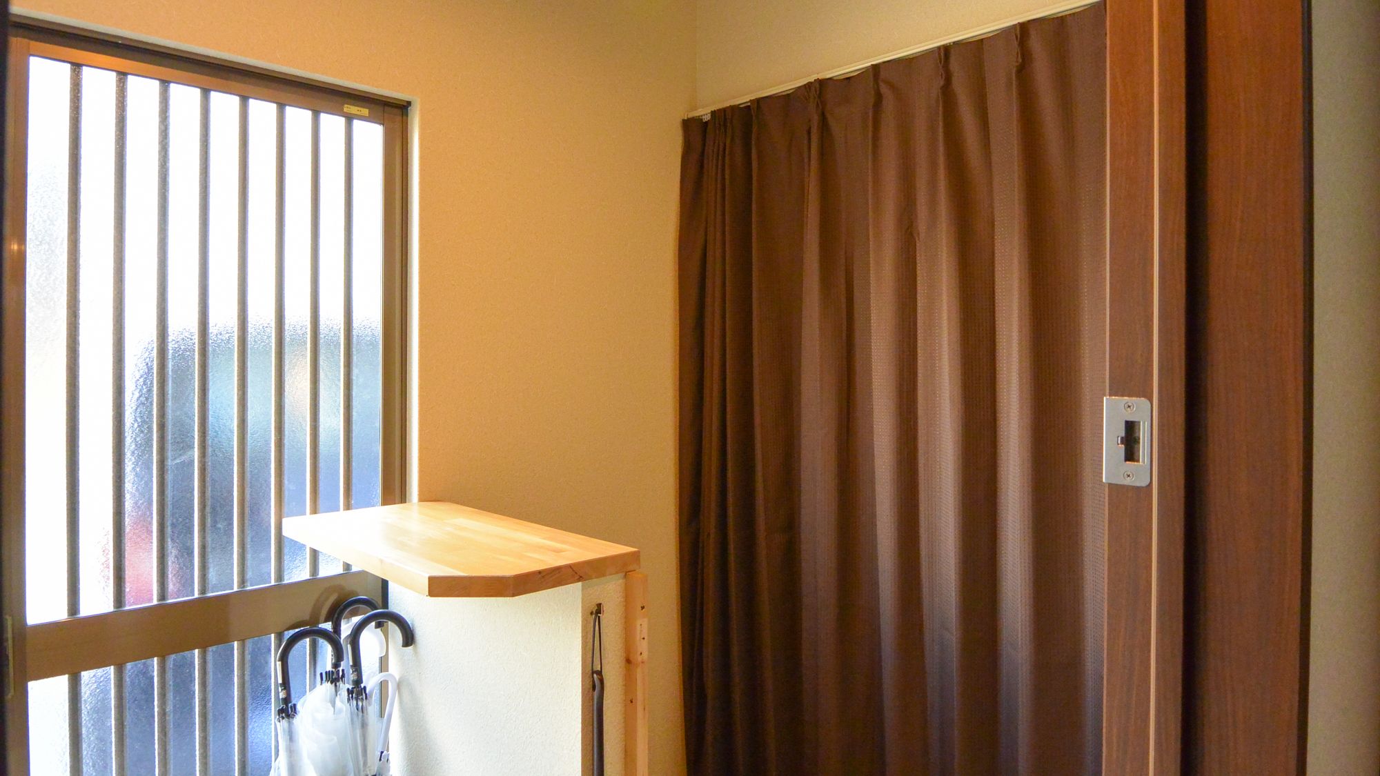 A room with a window, a curtain, and a wooden shelf.