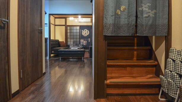 Ein traditionelles japanisches Interieur mit einer Holztreppe, Tatami-Bodenbelag und einem niedrigen Tisch mit Kissen.