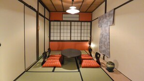 Ein traditioneller japanischer Raum mit Tatami-Bodenbelag, einem niedrigen Tisch mit Kissen und Shoji-Schirmwänden.
