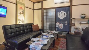 Ein traditioneller japanischer Wohnraum mit einem schwarzen Ledersofa, einem niedrigen Tisch gedeckt mit Geschirr und Gläsern, sowie einer Schiebetür mit dekorativem Feld.