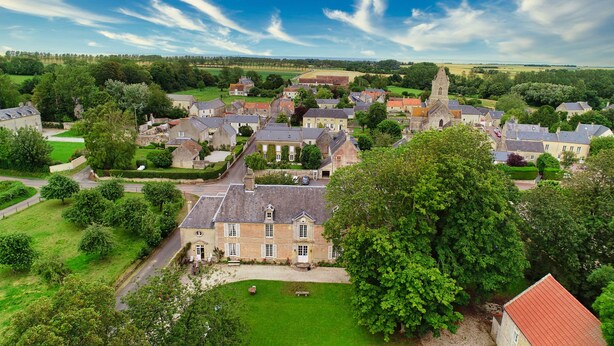 A historic village with traditional stone buildings, a central church, and surrounding green fields.