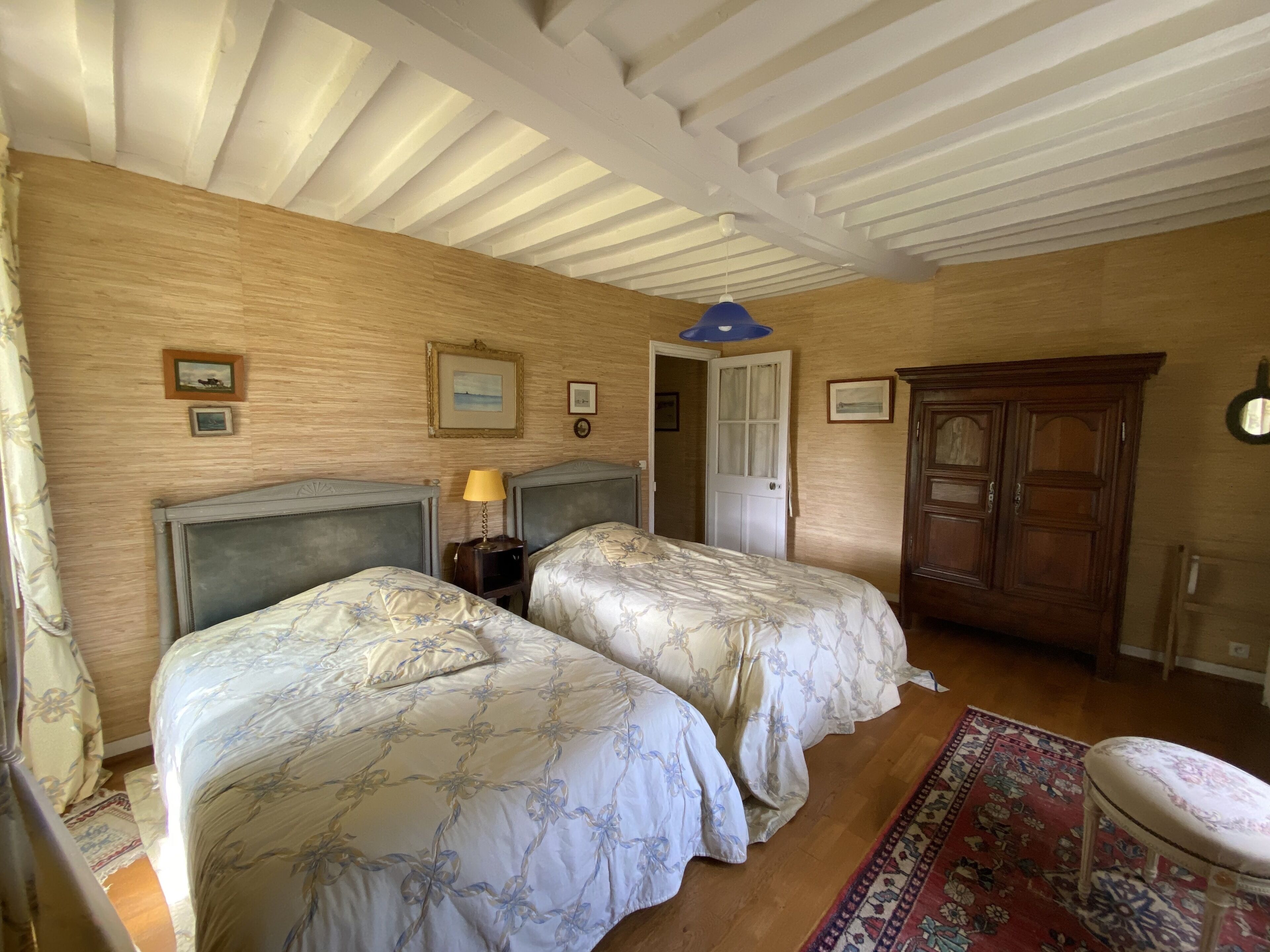 Una habitación con dos camas, un armario de madera, una mesita y una puerta que da a otra estancia.