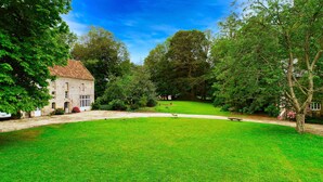 A stone building with a tiled roof, surrounded by a lush green lawn and trees.