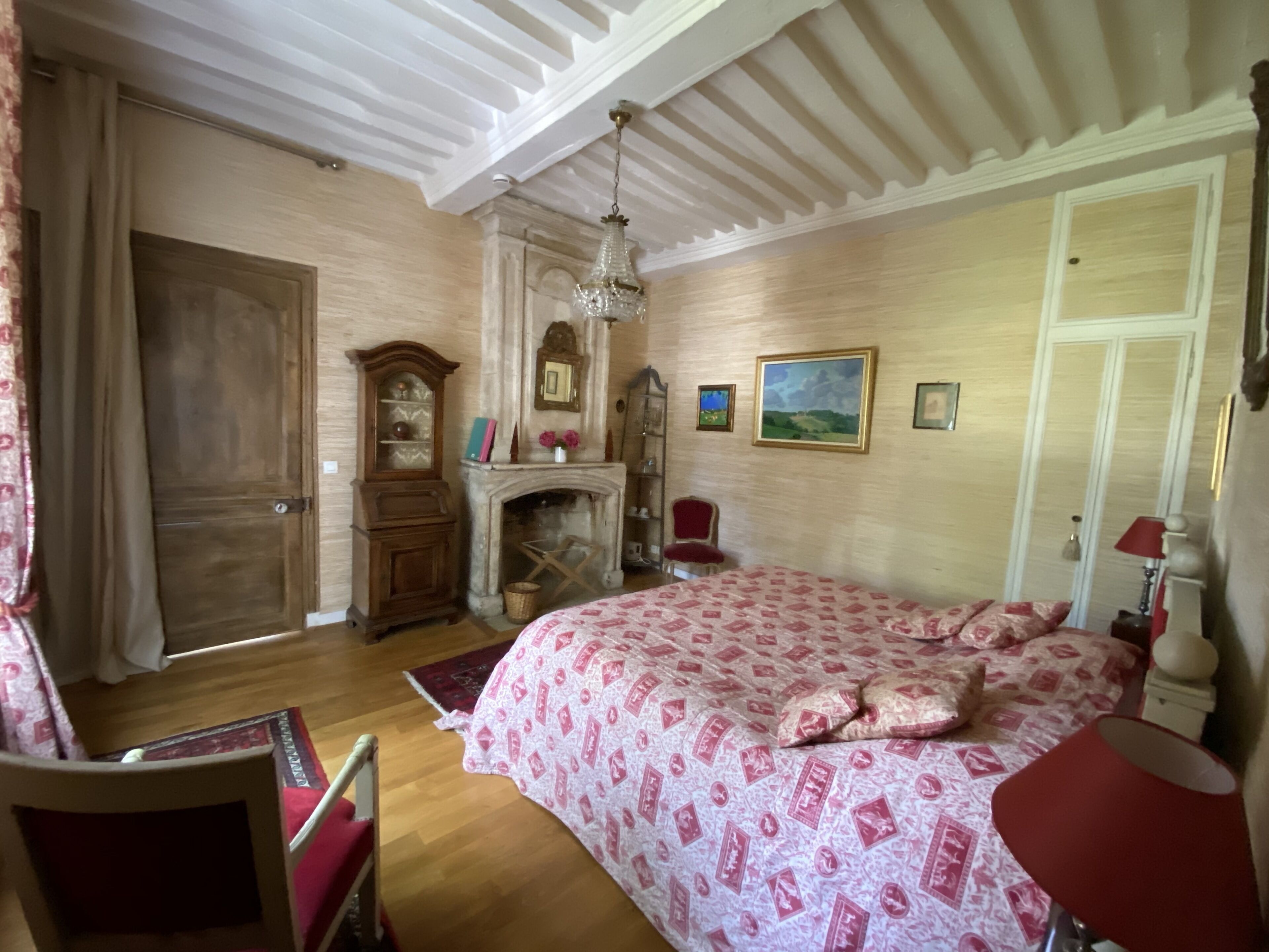 A bedroom with a large bed, a wooden wardrobe, a fireplace, and a chandelier.