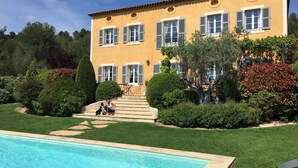 A large yellow building with multiple windows and shutters, surrounded by well-maintained lawns and a swimming pool.