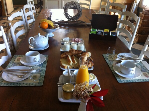 A breakfast setting with a variety of food items and drinks on a wooden table, surrounded by white chairs. - Bastide Tara (Cabries)