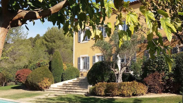 A poolside area with a clear view of a building with a yellow facade, a staircase leading to the entrance, and well-maintained greenery.