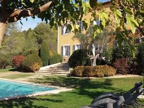 A poolside area with a clear view of a building with a yellow facade, a staircase leading to the entrance, and well-maintained greenery. - Bastide Tara (Cabries)
