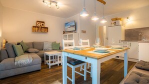 A modern living room with a grey sofa, a wooden dining table, and a kitchen area with white cabinets and a wooden countertop.