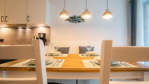 A dining area with a wooden table set for two, white chairs, and pendant lights above.