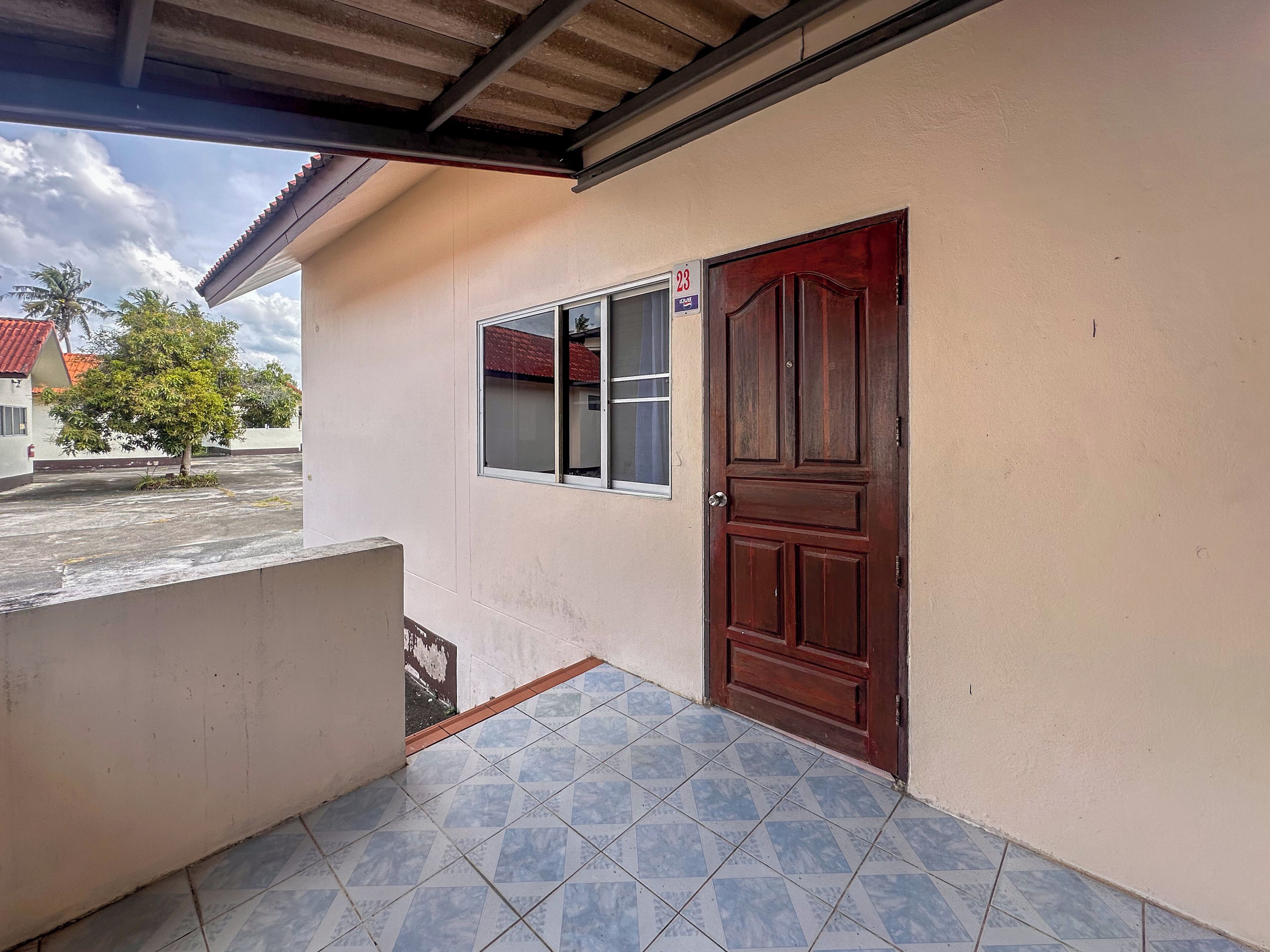 A building with a tiled porch, a wooden door, and a window with a sign.