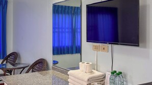 Een hotelkamer met een flatscreen televisie, een spiegel, een kleine tafel met stoelen, een stapel handdoeken en toiletartikelen.