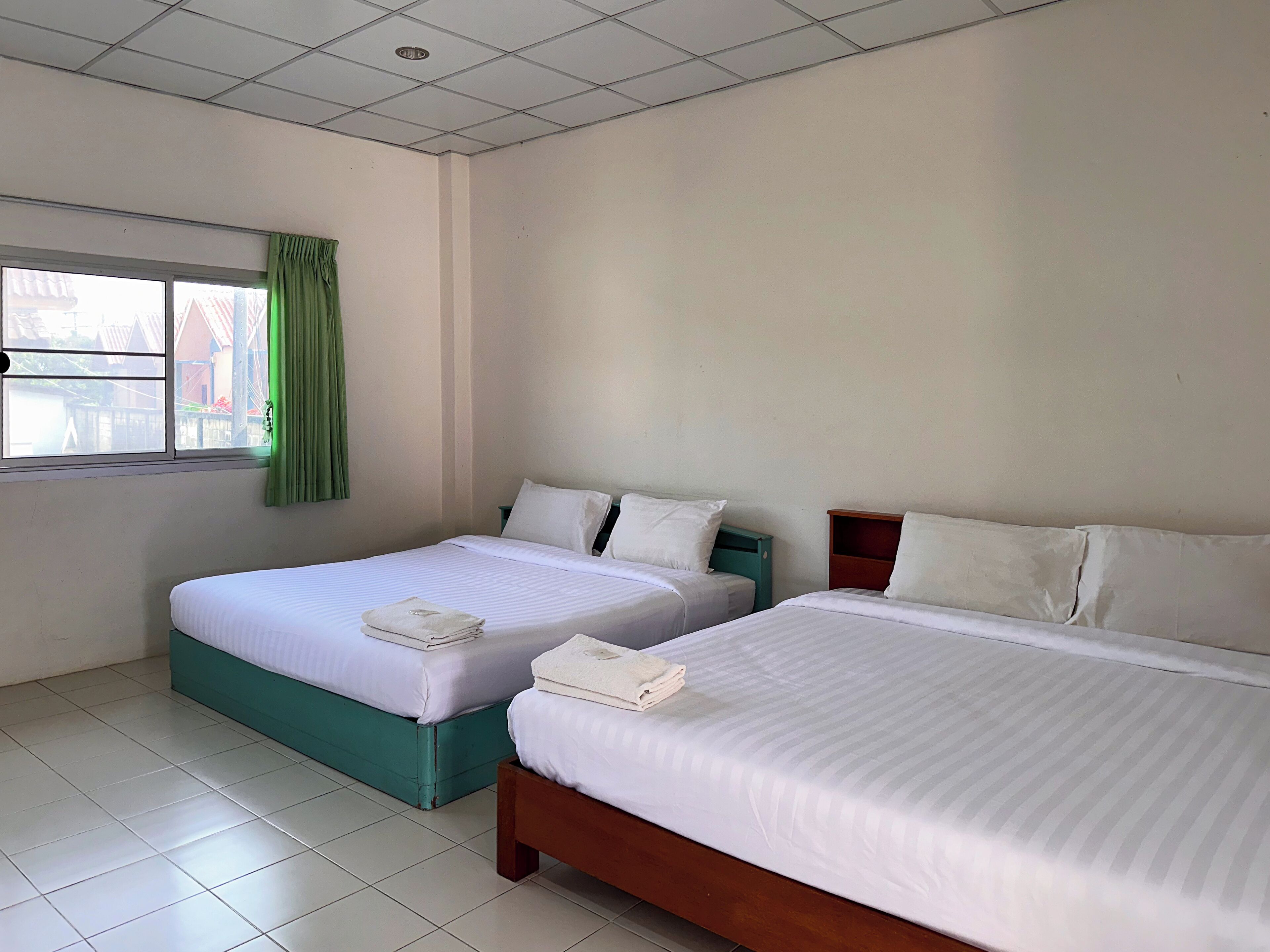 Une chambre d’hôtel avec deux lits, une fenêtre avec des rideaux verts et un sol carrelé.