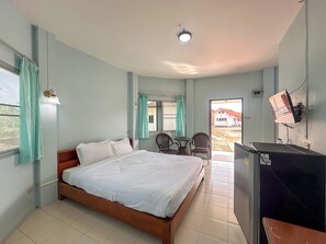 Un dormitorio con cama, escritorio, dos sillas, televisor y ventana con cortinas.