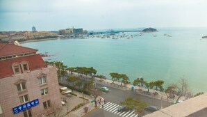 A coastal cityscape with a prominent building featuring a blue sign, a waterfront promenade, and a distant island with boats.