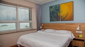 A bedroom with a large bed, a nightstand, a lamp, and a window with a view of a distant island.