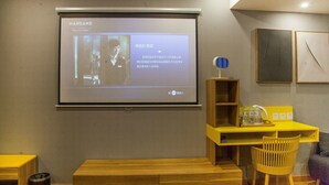 A conference room with a projection screen displaying a presentation, wooden furniture, and a yellow desk.