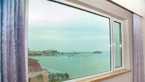 A view from a window overlooking a body of water with boats, buildings, and a distant island.