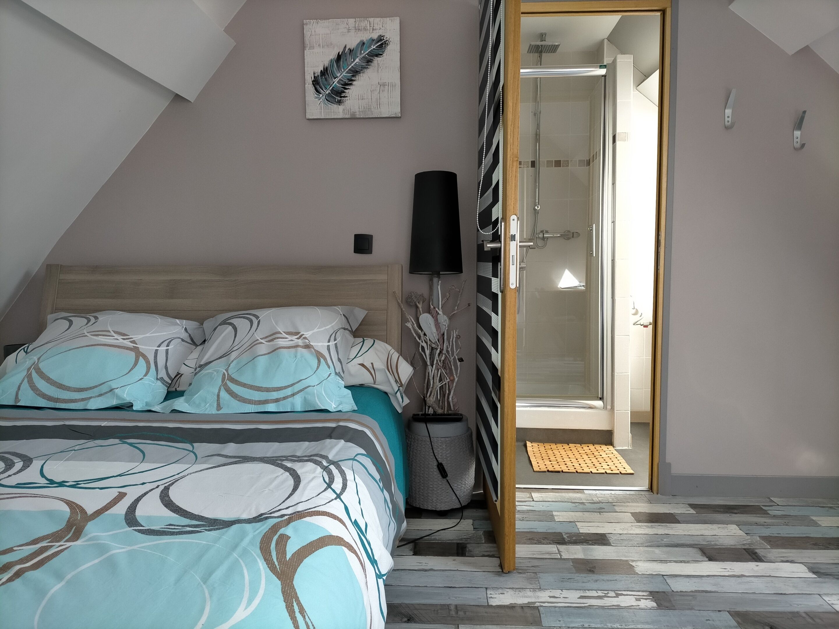 A bedroom with a bed, a bedside lamp, a shower, and a door leading to another room.
