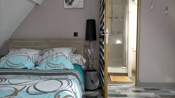 A bedroom with a bed, a bedside lamp, a shower, and a door leading to another room.