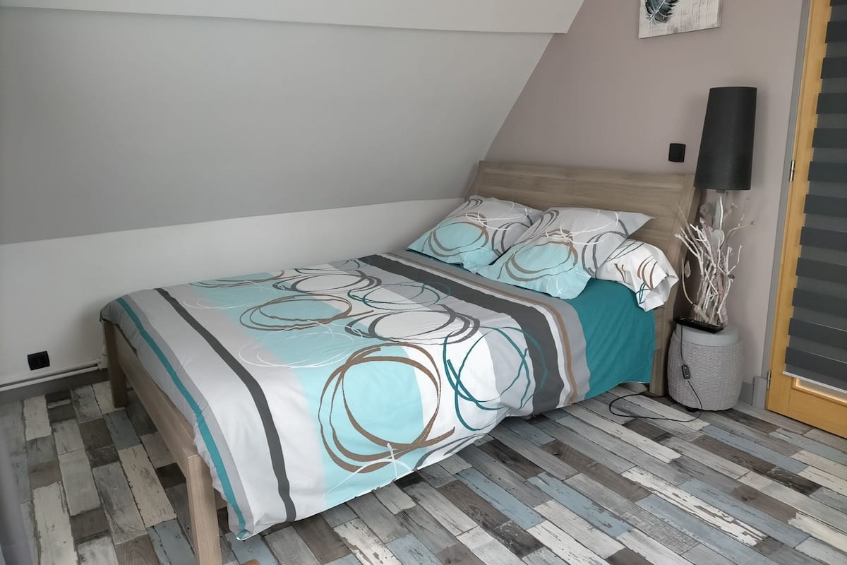A bedroom with a bed, a wall-mounted lamp, and a decorative plant.
