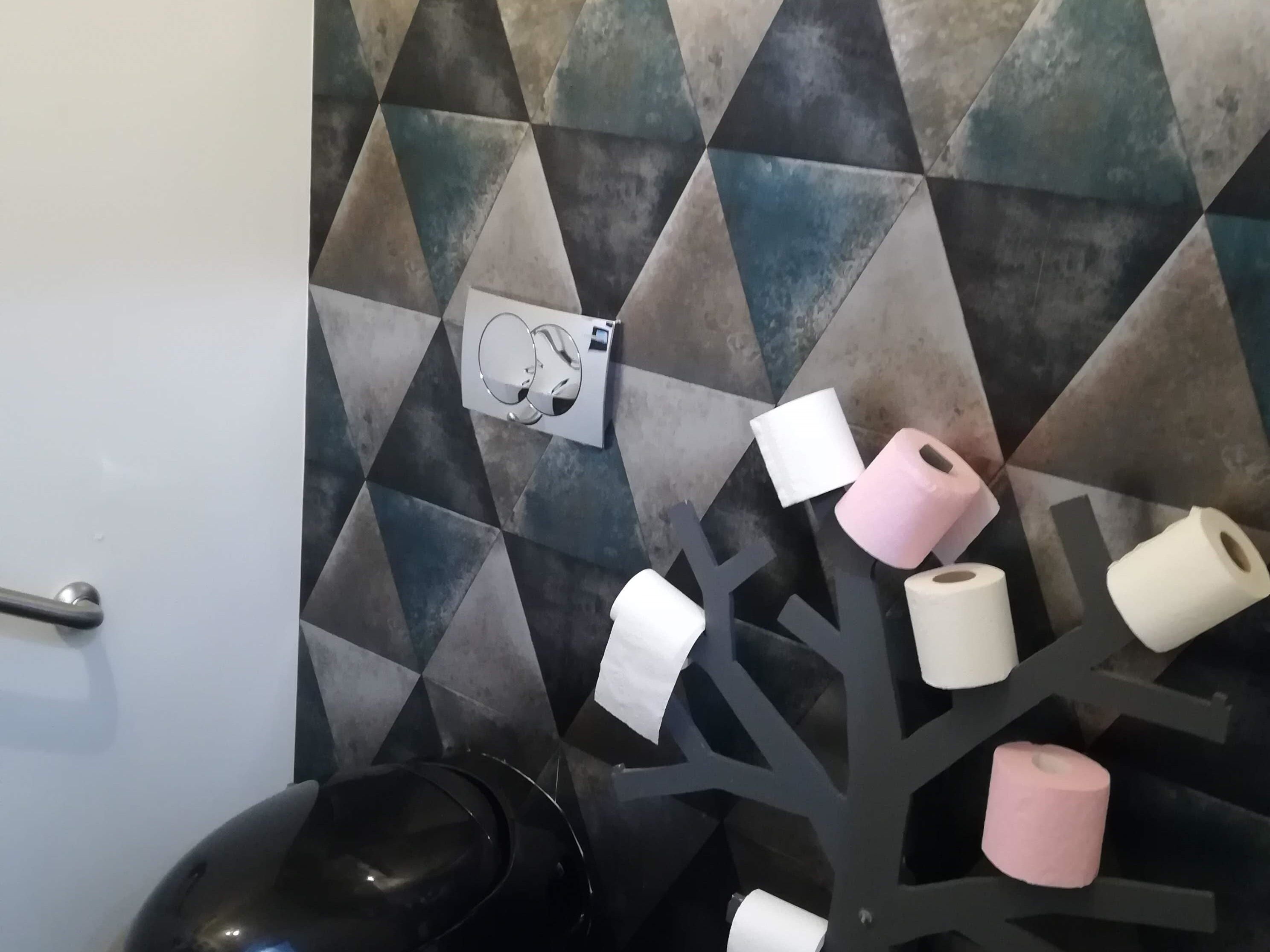Un baño con un salpicadero de azulejos geométricos y un dispensador de papel higiénico con rollos.