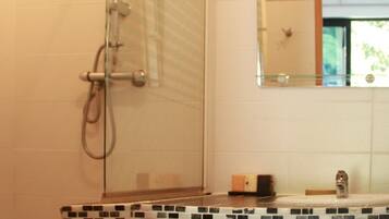 A bathroom with a shower, a sink with a tiled countertop, and a mirror.