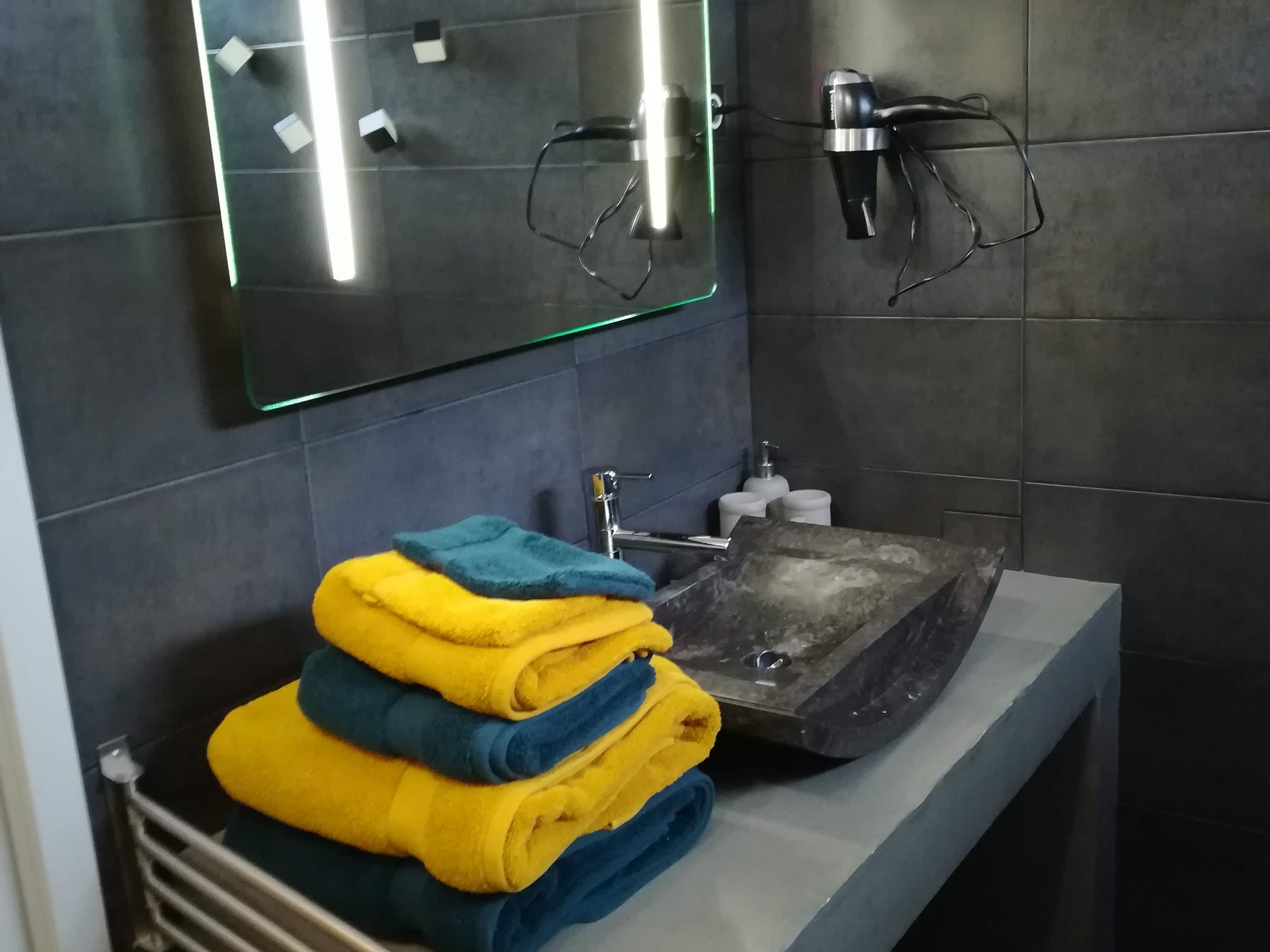 A modern bathroom with a glass-topped sink, dark tiles, and a stack of towels.