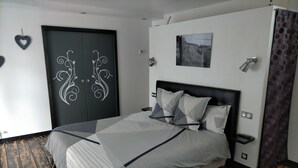 A modern bedroom with a large bed, a wardrobe with decorative doors, a small bedside table, and a wall-mounted light fixture. - Cléome (Arques-la-Bataille)