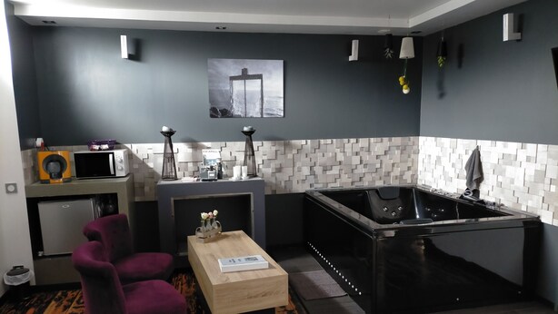 A compact kitchen with a microwave, toaster, and sink. There is a wooden table with a vase of flowers, a purple chair, and a black bathtub. - Cléome (Arques-la-Bataille)