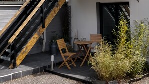 A two-story building with a wooden staircase leading to a balcony. There is a small outdoor seating area with a table and chairs. - Cléome (Arques-la-Bataille)