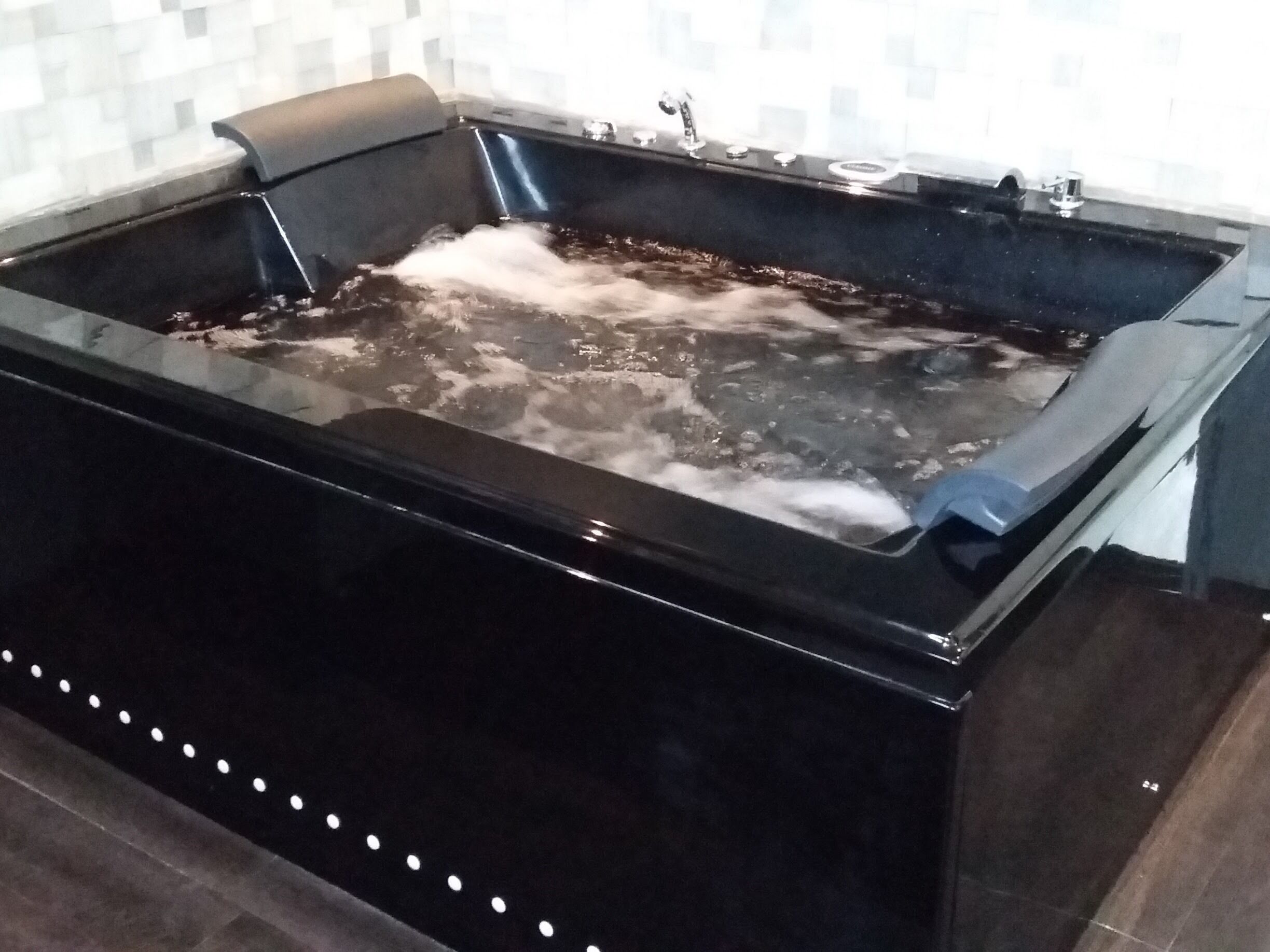 Una bañera de hidromasaje negra con burbujas visibles, un grifo y un panel de control.
