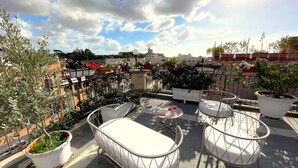 Eine Dachterrasse mit Sitzgelegenheiten im Freien, Blumentöpfen und Blick auf die Stadtlandschaft.
