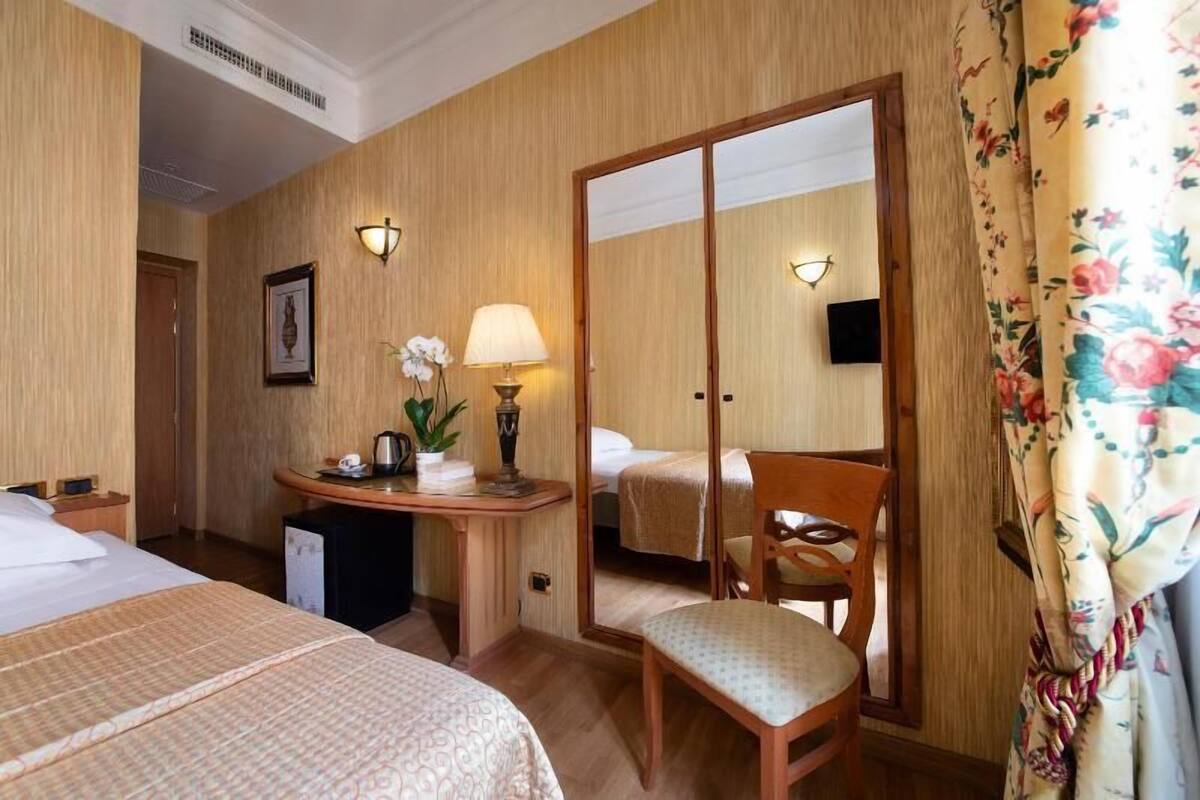 Une chambre d’hôtel avec deux lits, un bureau avec une lampe, une chaise et un miroir.