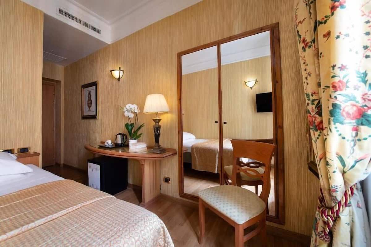 A hotel room with two beds, a desk with a lamp, a chair, and a mirror.