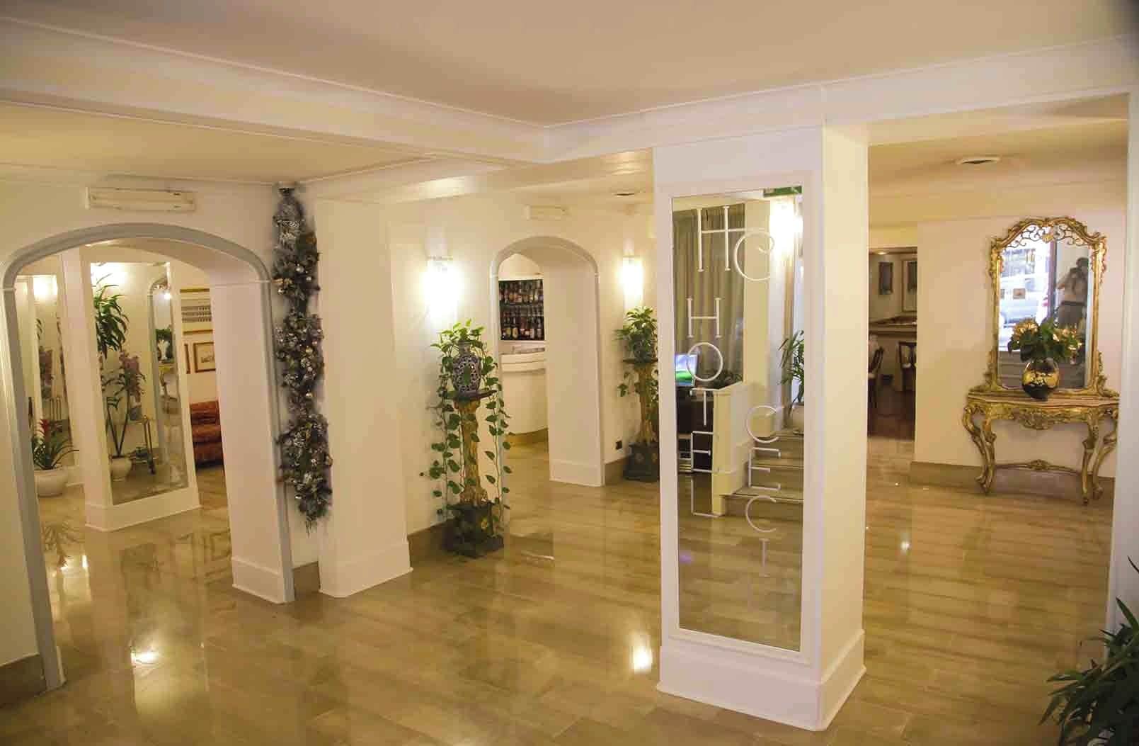 A spacious hotel lobby with a polished wooden floor, multiple arches, and potted plants.