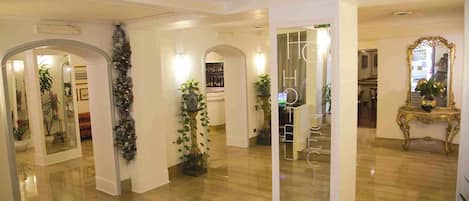 A spacious hotel lobby with a polished wooden floor, multiple arches, and potted plants.
