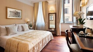 Ein Hotelzimmer mit einem großen Bett, einem Schreibtisch mit Stuhl, einem Spiegel und einem Fenster mit Vorhängen.