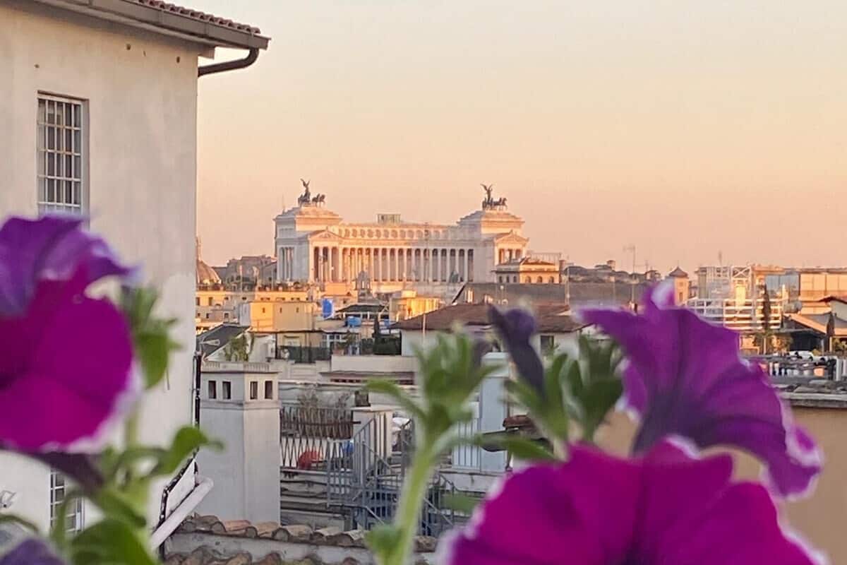 Un bâtiment à l’architecture classique, avec des colonnes et des statues, et une vue sur le paysage urbain en arrière-plan.