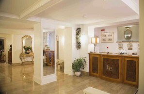 A hotel lobby with a reception desk, a mirror, a potted plant, and a wall-mounted lamp. - Hotel Cecil (Rome)