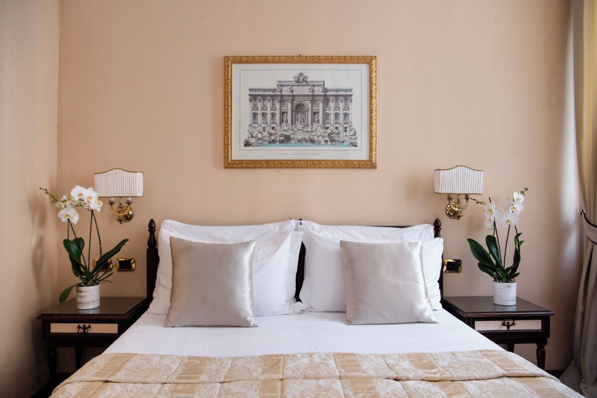 A hotel room with a large bed, two nightstands, a framed picture on the wall, and two potted orchids.