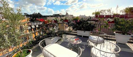 A rooftop terrace with outdoor seating, potted plants, and a city view.
