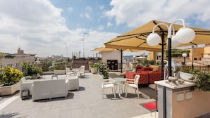 A rooftop terrace with outdoor seating, a large umbrella, and a view of the cityscape. - Hotel Cecil (Rome)