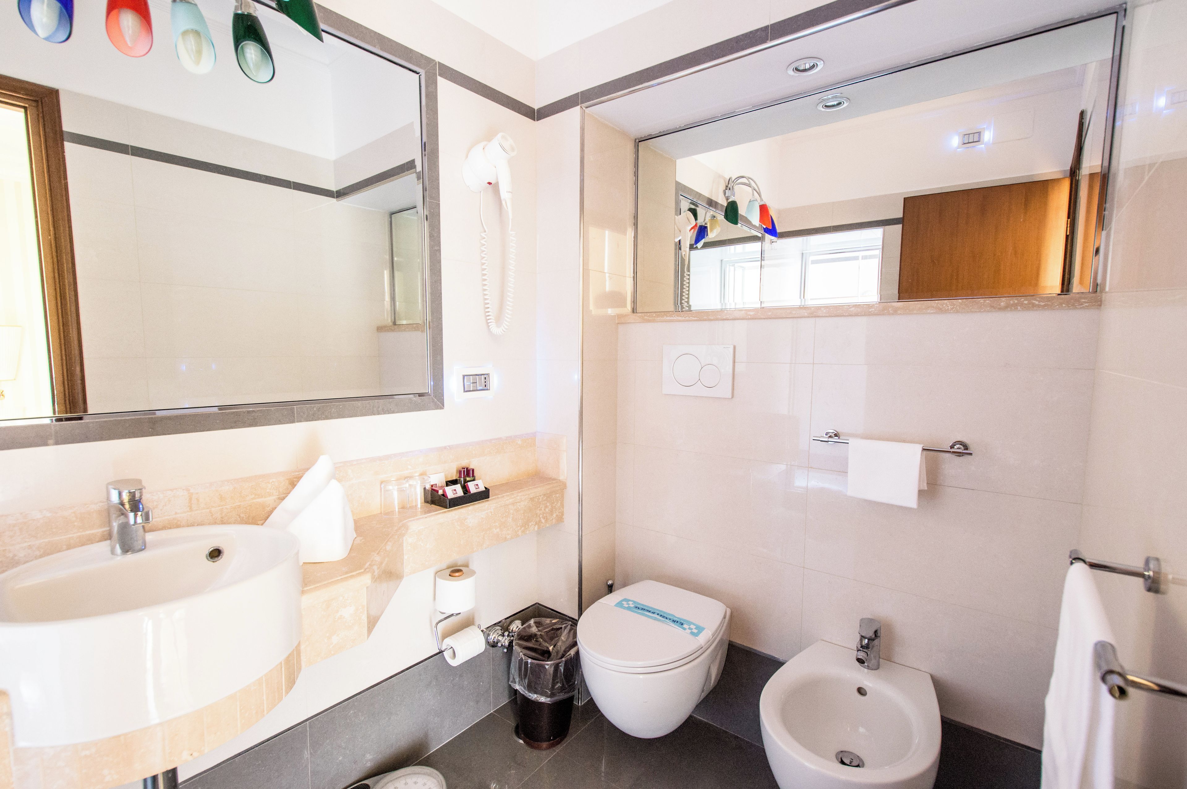 A modern bathroom with a sink, toilet, bidet, and a large mirror.
