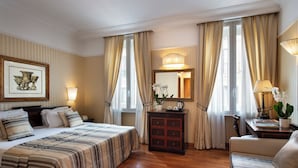 A hotel room with a large bed, a sofa, a desk with a lamp, a dresser, and a large mirror. - Hotel Cecil (Rome)