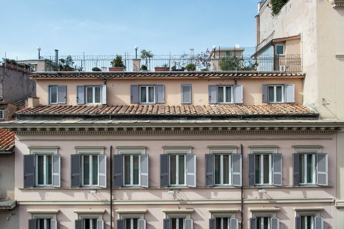 A multi-story building with a consistent architectural style, featuring a series of windows with shutters, a tiled roof, and balconies.