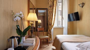Una habitación de hotel con cama, escritorio con lámpara, silla, televisor y ventana con cortinas.